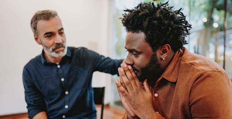 A Black man and a White man sit together, engaged in a serious conversation