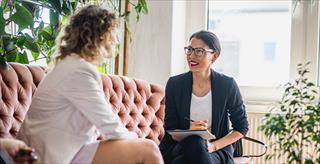 A mental health professional sitting and talking with a woman on a couch