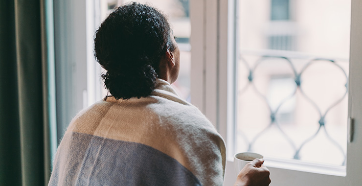 woman holding a coffee mug lookiing out a wiindow