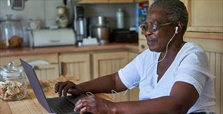 Elderly woman with headphones looks her computer