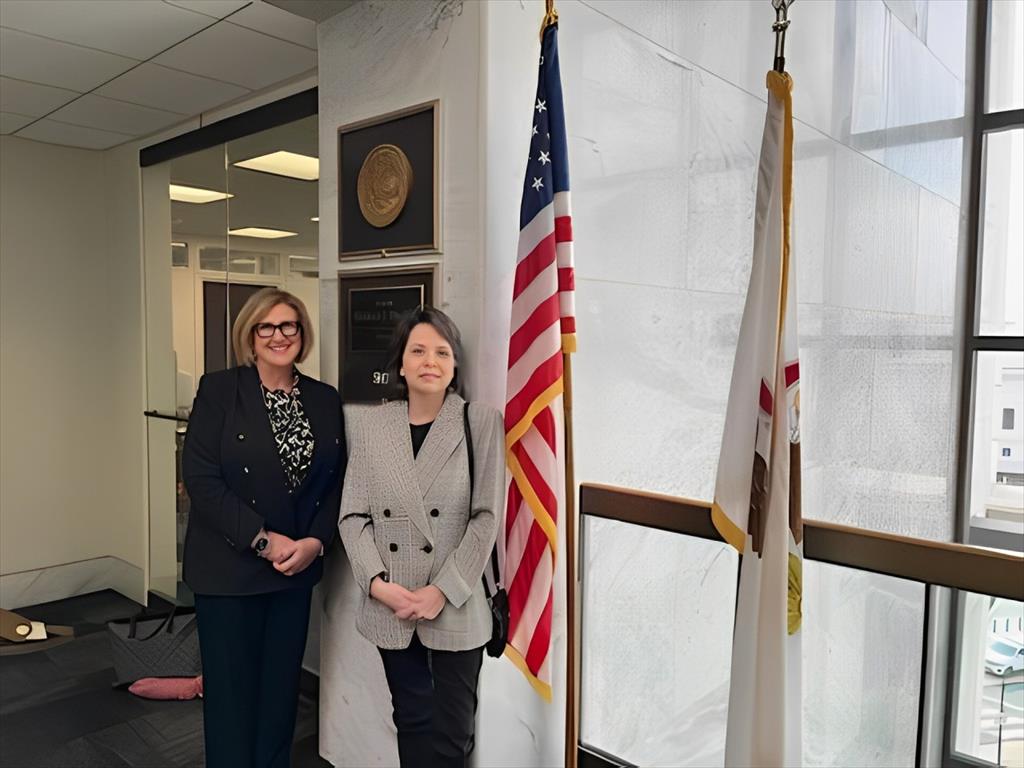 Laura Faynor-Ciha, PhD, and Mary Cashel, PhD, in an office building standing next to the American Flag