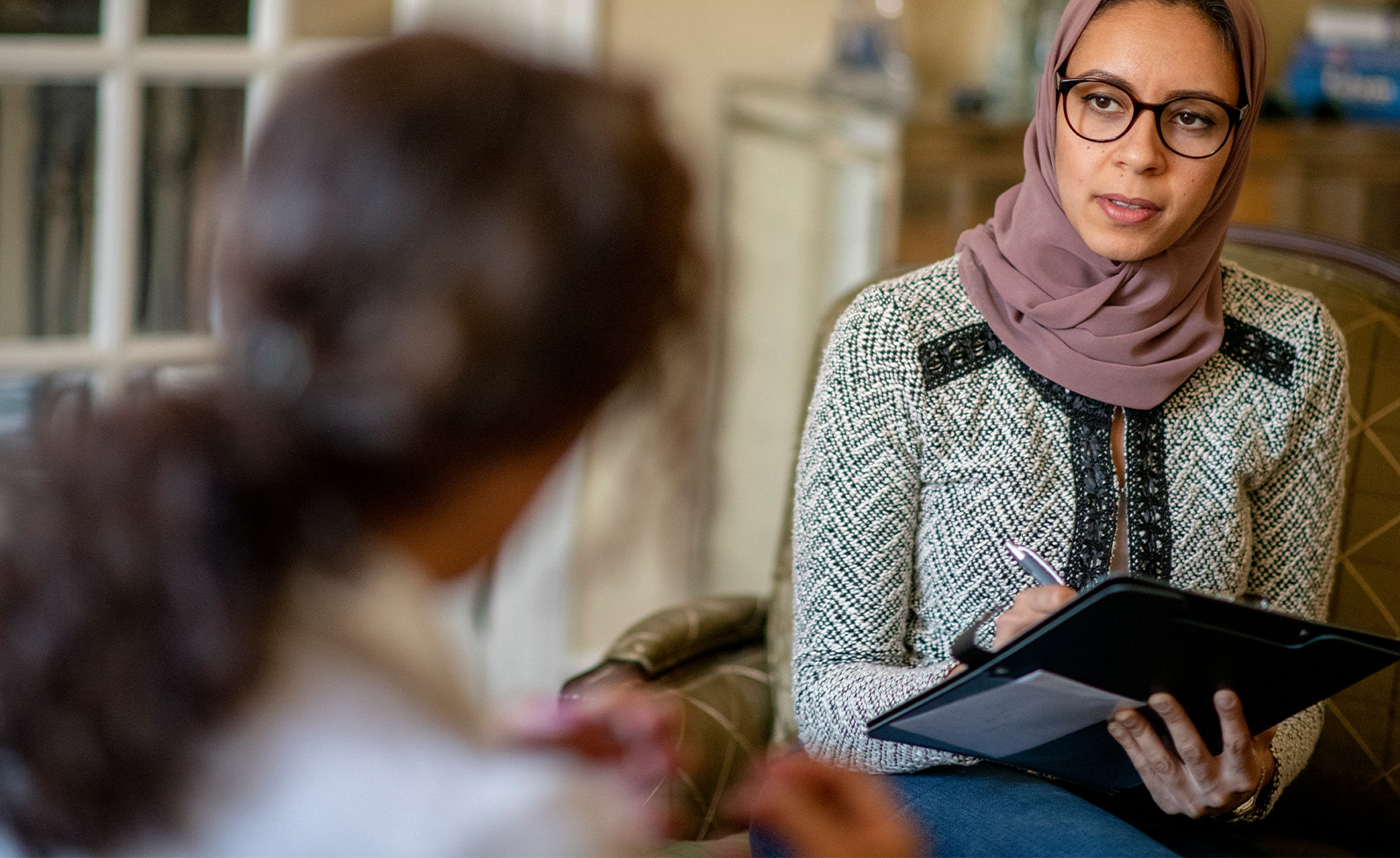 A middle age professional woman is taking notes and talking to her client on a couch