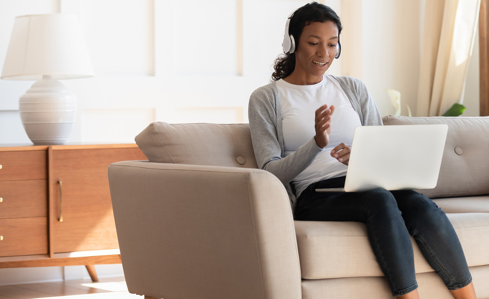 Black woman sitting on the couch wearing headphones and working on a laptop