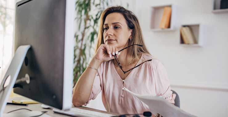 Woman holding her glasses while looking at computer screen