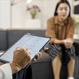Clinician holds a digital tablet while a patient sits on a sofa.