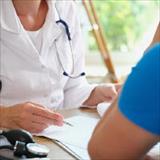 Healthcare professional with a stethoscope consulting with a patient across a desk in a medical office.