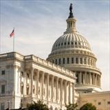 View of the U.S. Capitol building dome and American flag against a clear sky.
