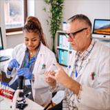 Two healthcare researchers in lab coats review clinical trial samples at a laboratory workstation.