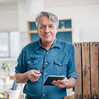 Man holding eyeglasses and a tablet