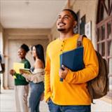 Students gather and talk in a campus walkway while a student in the foreground carries folders and a backpack.