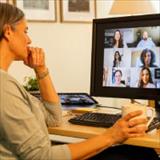 Woman seated at a home office desk participating in a video conference on a computer monitor.