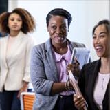 Professional women socializing in a workplace office while holding notebooks and materials.