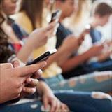 A group of children sitting in a row of chairs, engrossed in their cell phones
