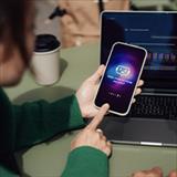Woman pointing to her smartphone displaying a chat interface and a laptop with data visualizations