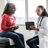 A female doctor shows a female patient information on a tablet