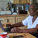 Elderly woman with headphones looks her computer