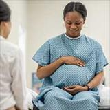 A young pregnant woman sit up on an exam table in her doctors office during a routine prenatal check-up