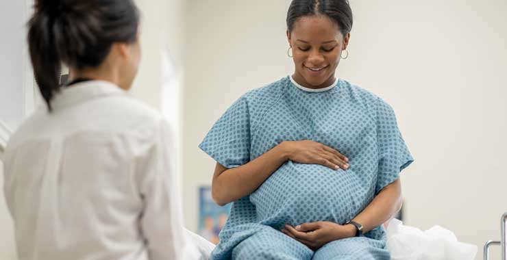 A young pregnant woman sit up on an exam table in her doctors office during a routine prenatal check-up
