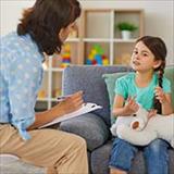 Happy little girl telling story to child psychologist during therapy session in cozy modern office