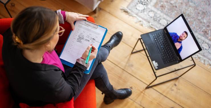 Above shot of a mental health professional taking notes during an online therapy session with a male patient