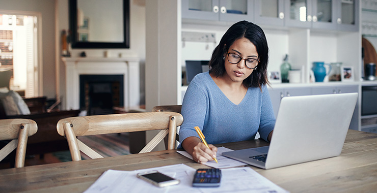 Woman sitting at a table with a laptop, notepad, and calculator