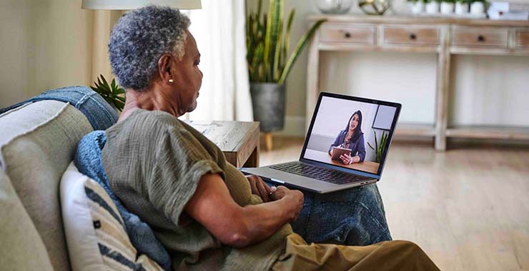 An older adult participates in a video call with a healthcare professional on their laptop