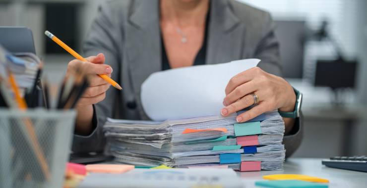 A person seated at a desk reviews a thick stack of documents.