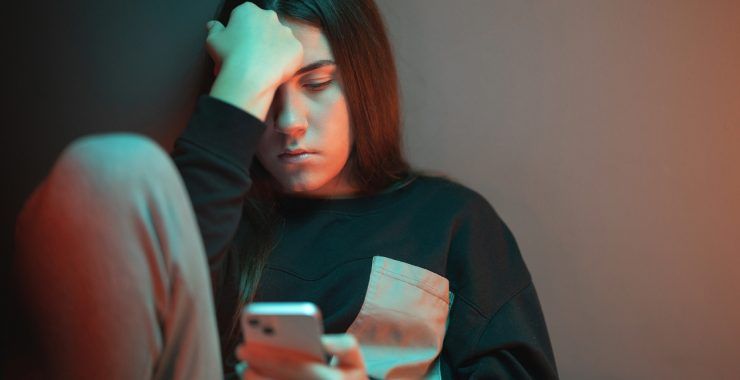 A woman in a depressed state of mind looks at her cell phone with a somber expression