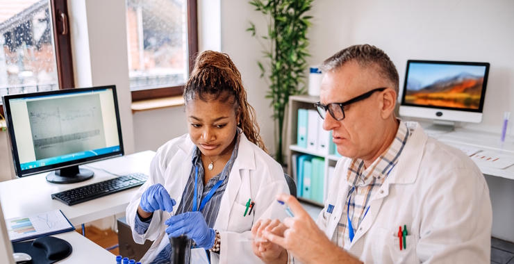 Two healthcare researchers in lab coats review clinical trial samples at a laboratory workstation.