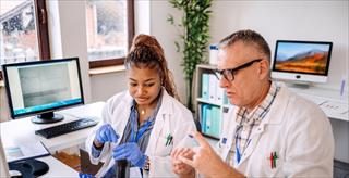 Two healthcare researchers in lab coats review clinical trial samples at a laboratory workstation.