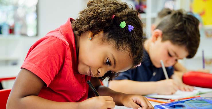 Two elementary school kids in class writing in their notebooks