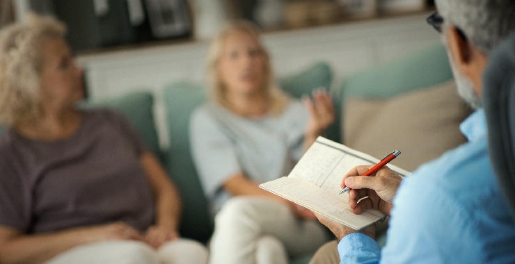 Psychologist takes notes while speaking with patients in a counseling session.