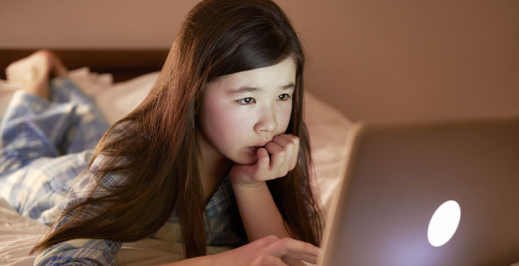 A young girl in her bed, looking at her laptop
