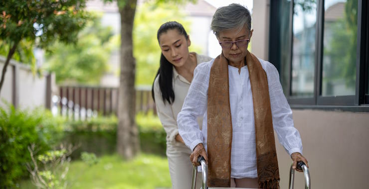 A younger woman assists an older woman using a walker