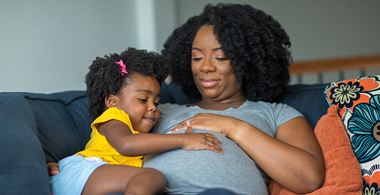Pregnant mother sitting with her daughter on a couch