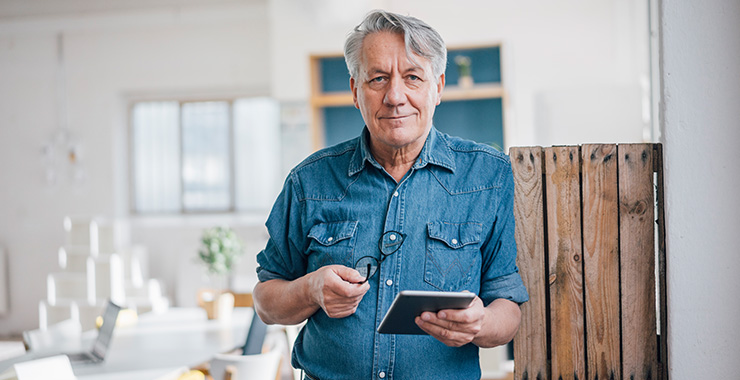 Man holding eyeglasses and a tablet