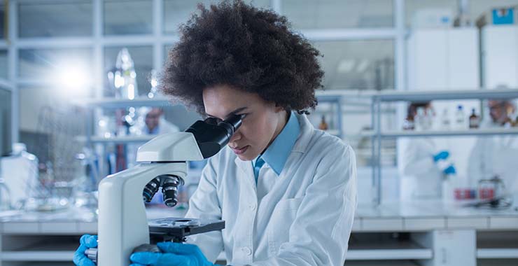 A female scientist in a lab looking through a microscope