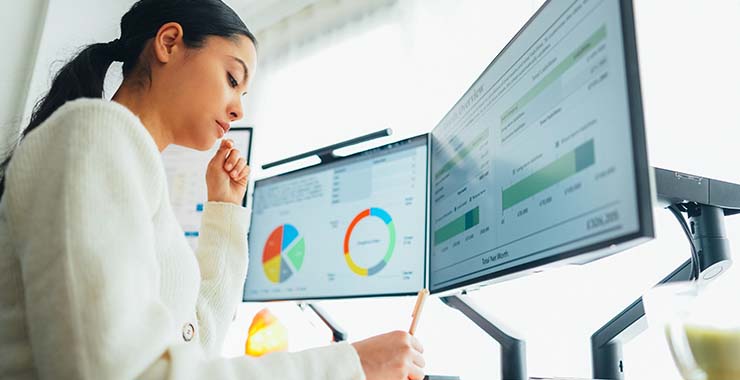 A woman analyzing charts on two computer screens