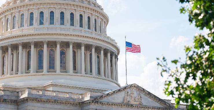A close-up view of the U.S. Capitol’s dome with an American flag waving in the foreground.