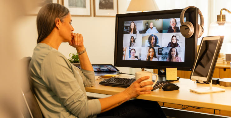 Woman seated at a home office desk participating in a video conference on a computer monitor.