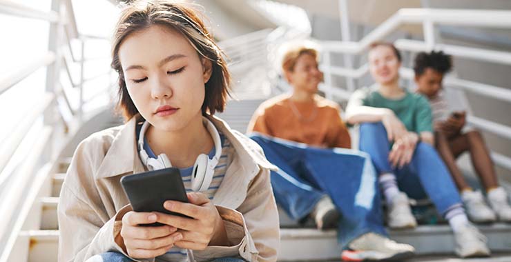Teenage girl looks at phone while kids laugh behind her