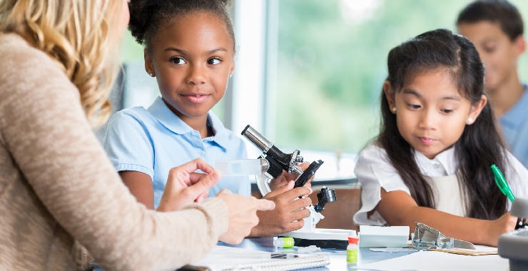 Children participate in a classroom science activity while examining a microscope with an instructor.