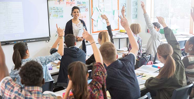 A classroom of high school students attentively raising their hands to participate in the lesson