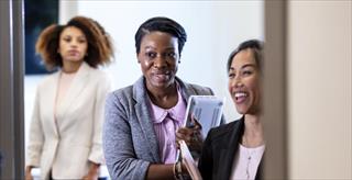 Professional women socializing in a workplace office while holding notebooks and materials.