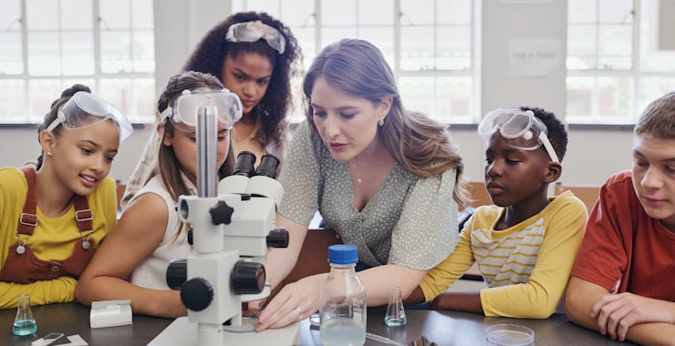 A teacher using a microscope, surrounded by her students