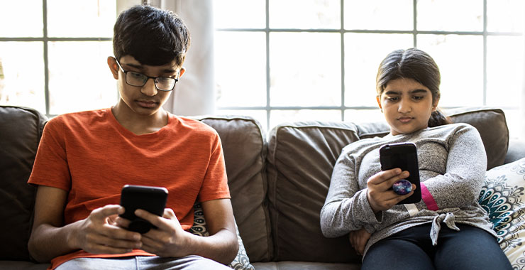 Two kids sitting on a coach staring at their phones