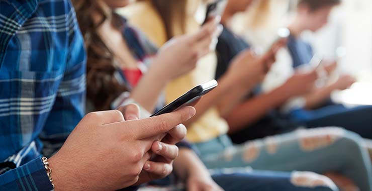 A group of children sitting in a row of chairs, engrossed in their cell phones
