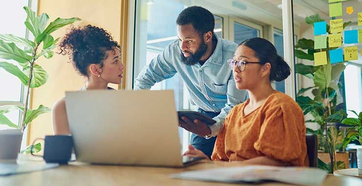Coworkers gathered around a laptop in an office, engaged in discussion and collaboration