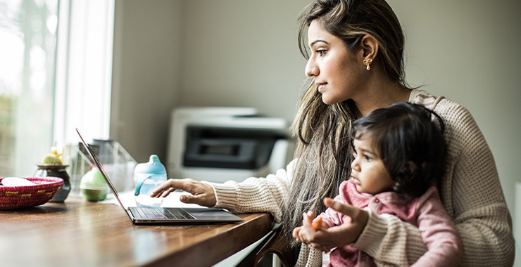 A mother using a laptop and holding her baby