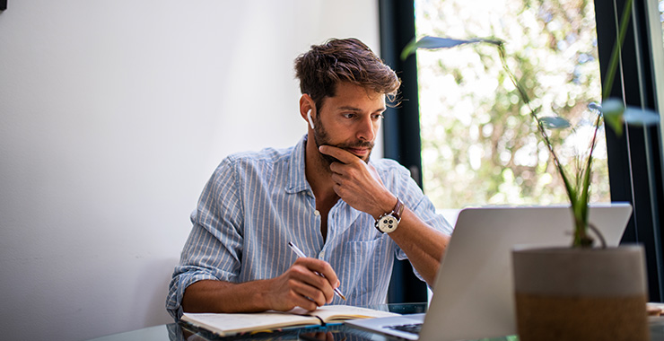 Man working at a desk with a notepad and laptop